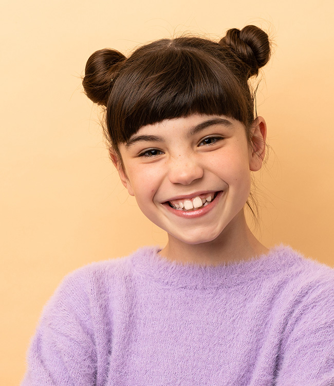 Mädchen mit dunklen Zöpfen lächelt in die Kamera -Symbolbild für Kinderzahnheilkunde in der Zahnarztpraxis Kowadent in Gerderath